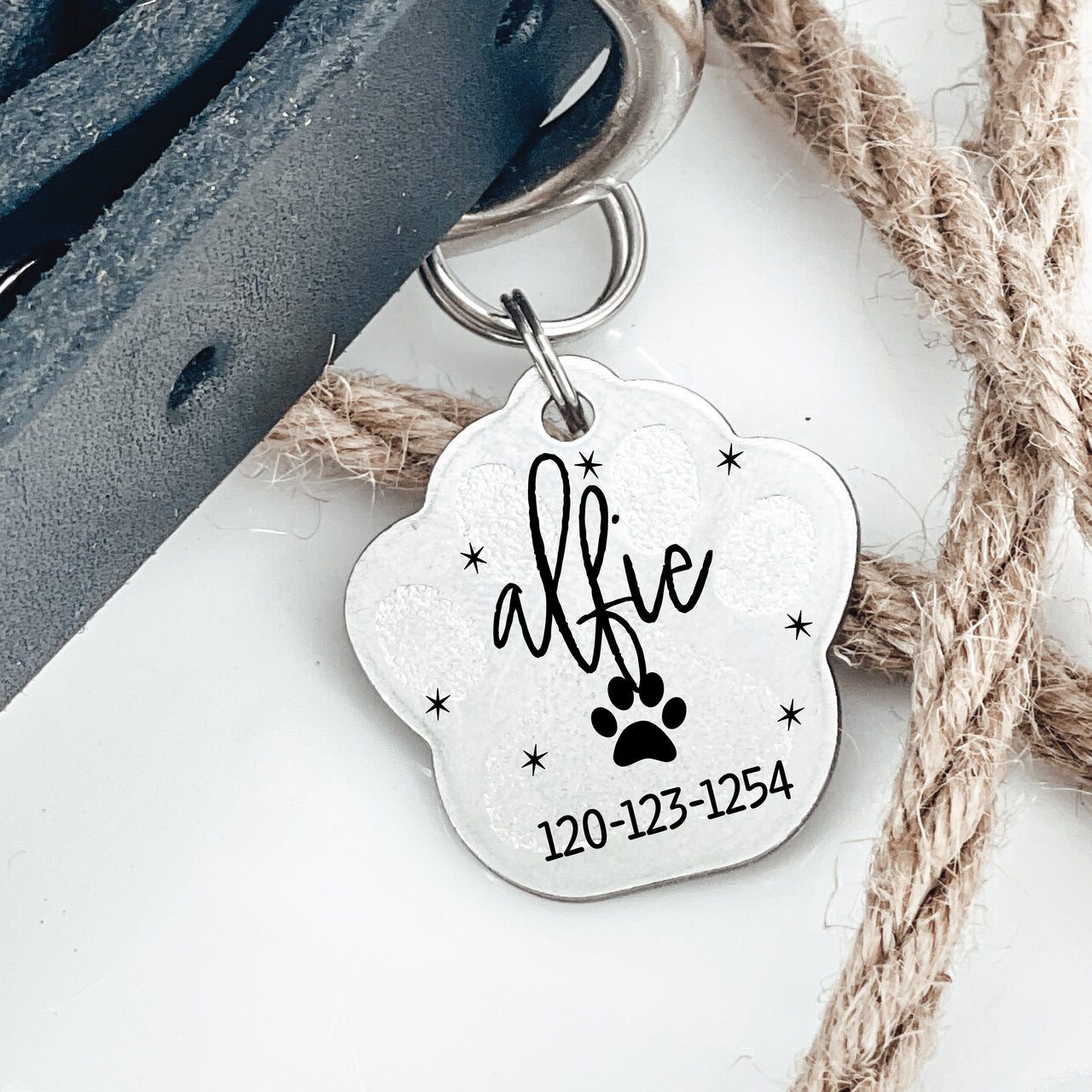 Silver pawprint shaped pet tag joined to collar by two jump rings. Tag has a pawprint, animal name, phone number engraved on it.