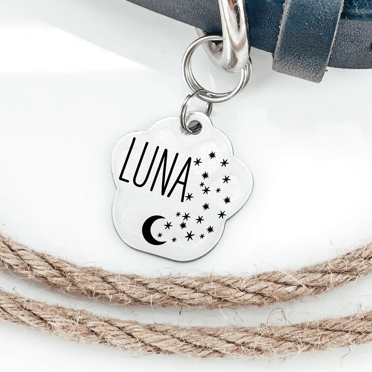 Silver pawprint shaped pet tag joined to collar by two jump rings. Tag has stars, a moon and animal name engraved on it.